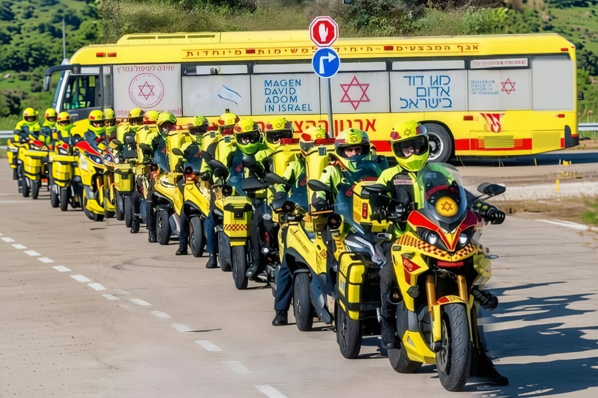 Magen David Adom medicycle responders in yellow gear lined up beside an MDA bus