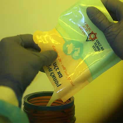 Gloved hands pour donor milk from a Magen David Adom milk bank bag into a jar